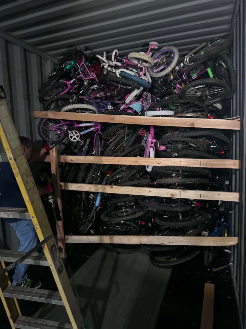 A volunteer on a ladder building wooden shelving inside a shipping container to hold the bicycles.
